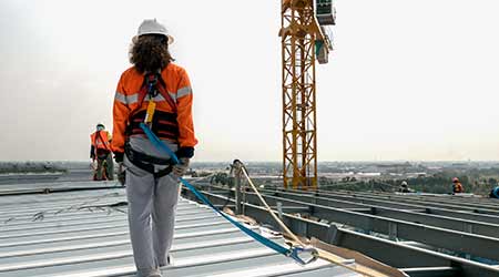 Construction worker wearing safety harness and safety line working on a metal industry roof new warehouse                                             